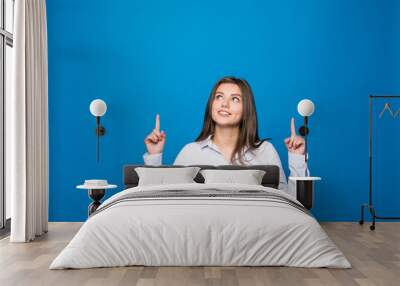 Smiling young woman pointing finger up over blue background Wall mural